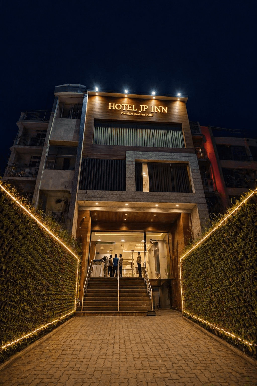 Illuminated Hotel JP Inn exterior at night with a cobblestone path between glowing green hedges.