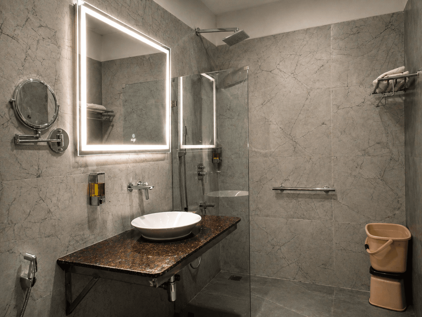 Modern grey marble bathroom with a lighted mirror, white vessel sink, and glass shower.