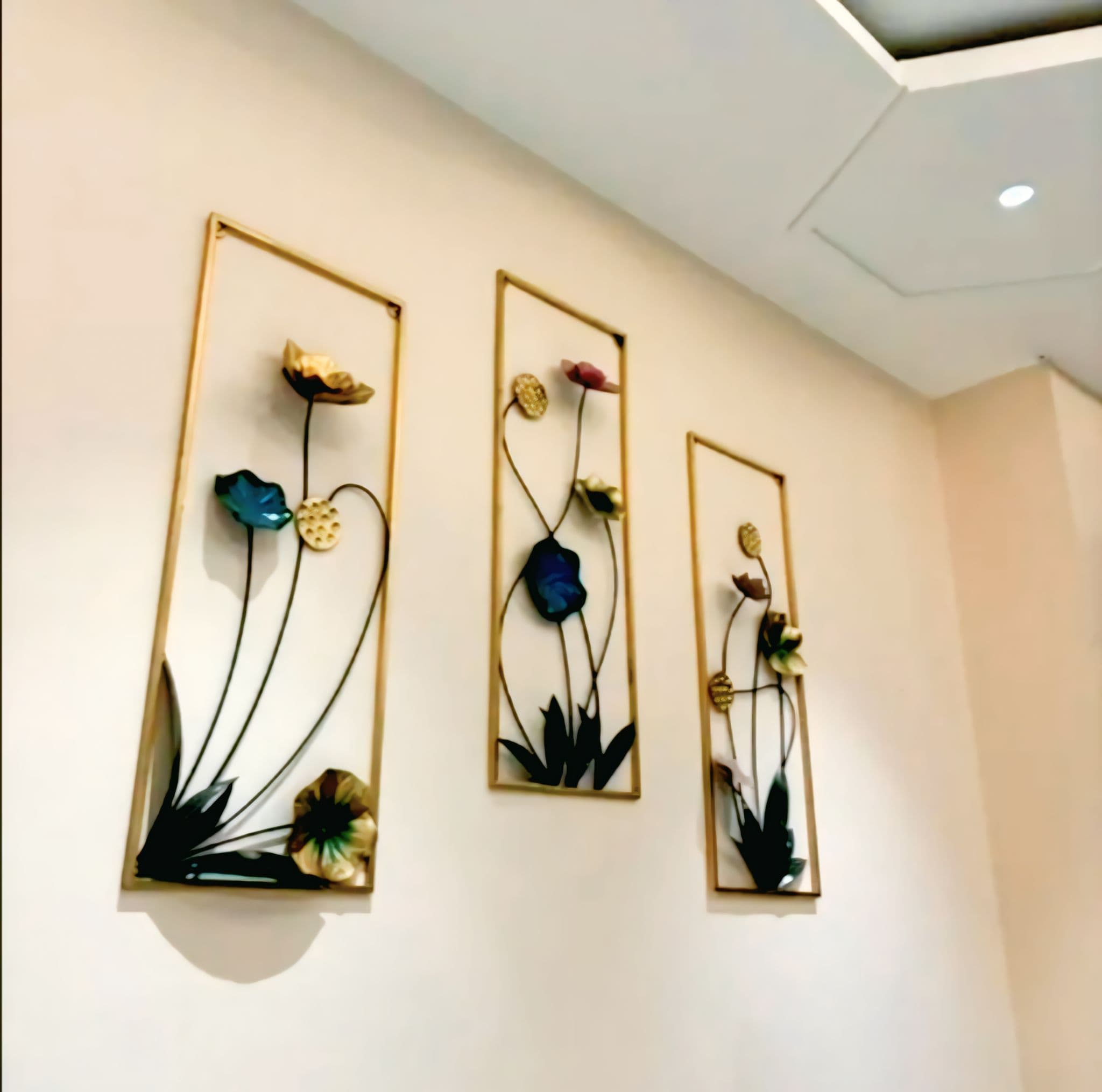 Three vertical gold frames featuring colorful metal lotus flower sculptures on a neutral wall.