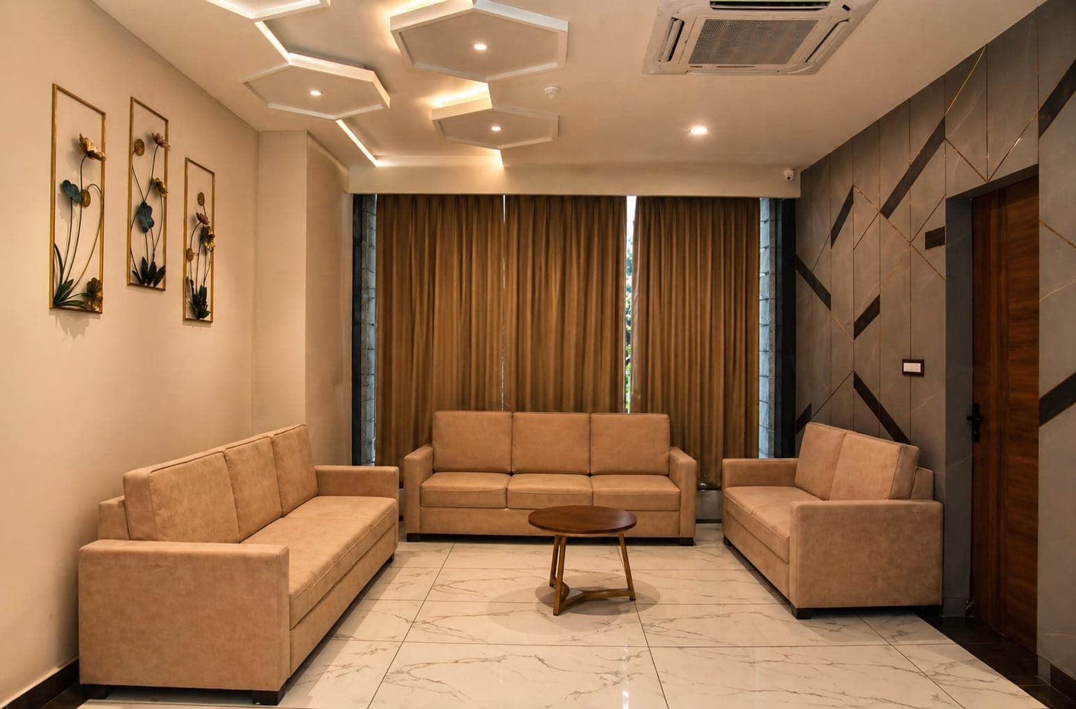 Modern lounge with tan sofas, marble floors, hexagonal ceiling lights, and gold wall art.