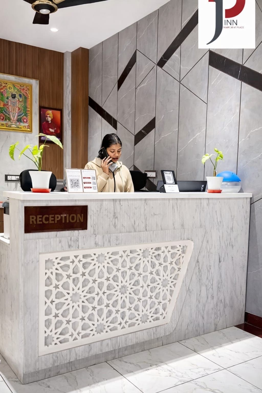 Receptionist talking on a phone behind a white marble desk with decorative lattice patterns.