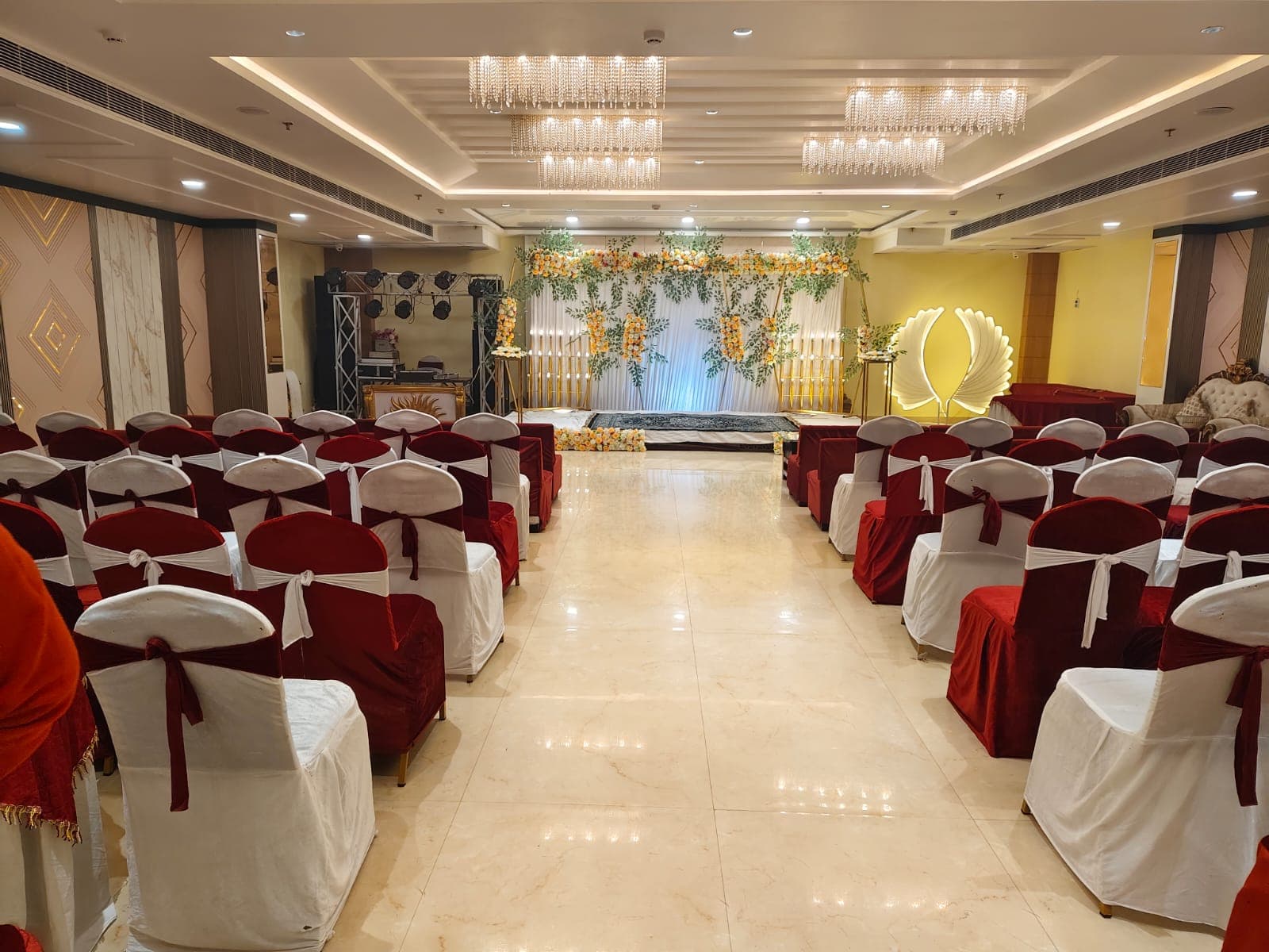 Crystal chandeliers illuminate rows of red and white chairs facing a floral stage.