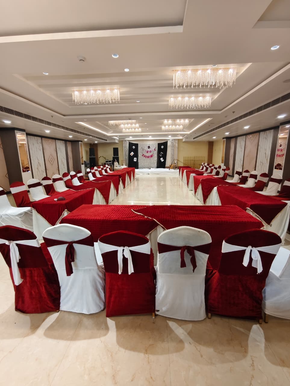 Elegant banquet hall with red velvet tables and white chairs under multiple crystal chandeliers.