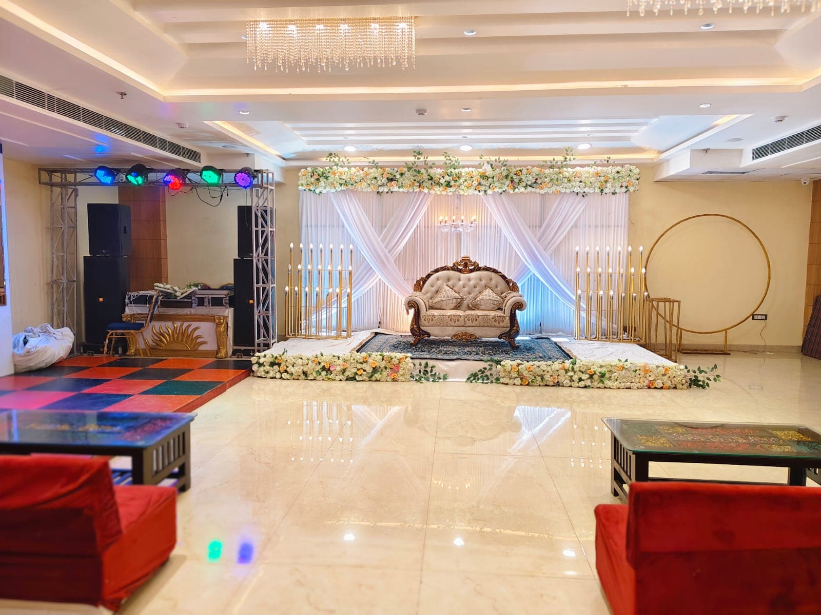 Ornate white sofa on a floral-decorated stage with white drapes and golden candle-like fixtures.