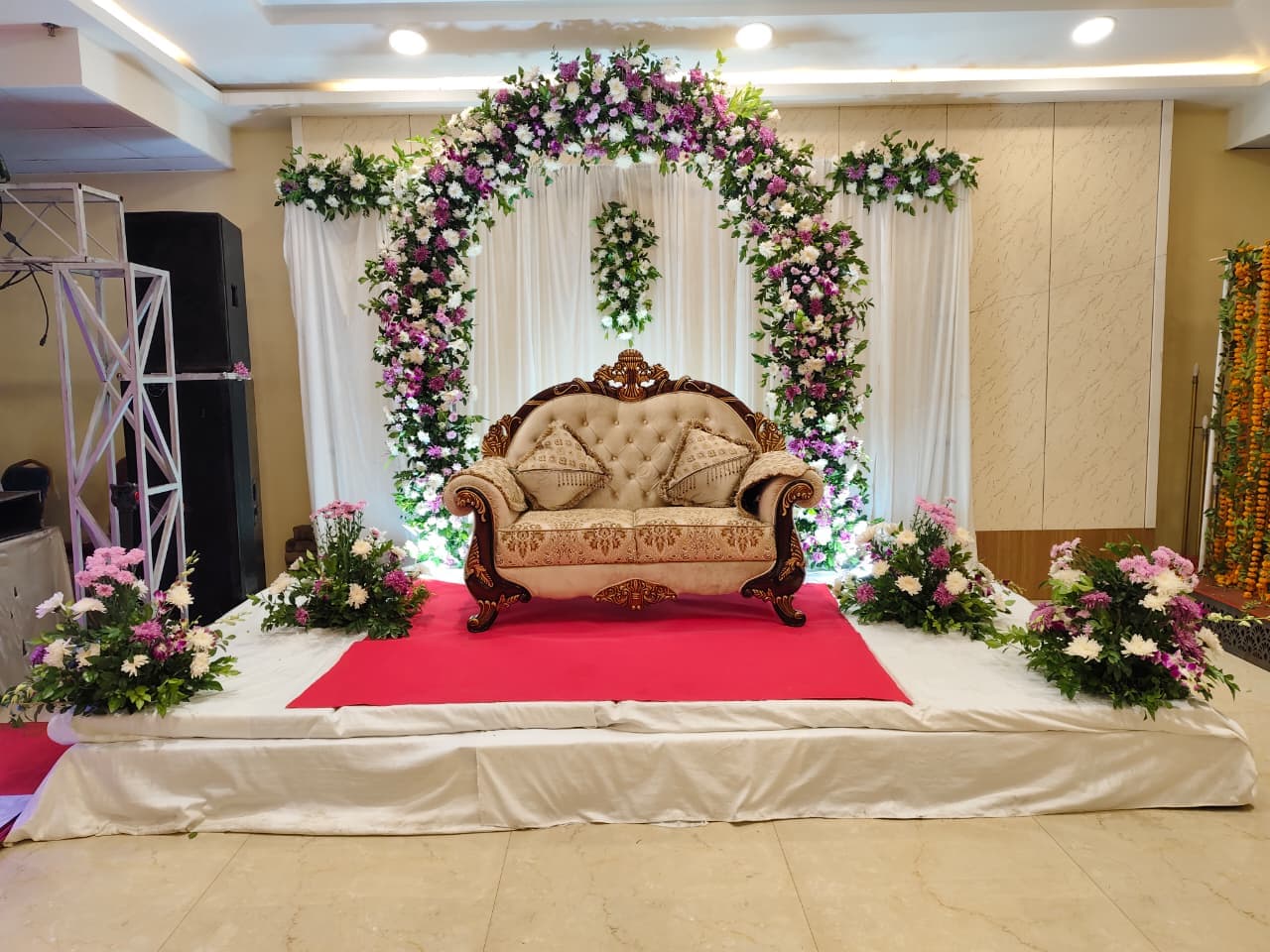 Ornate cream sofa on a red carpet under a purple and white floral arch.