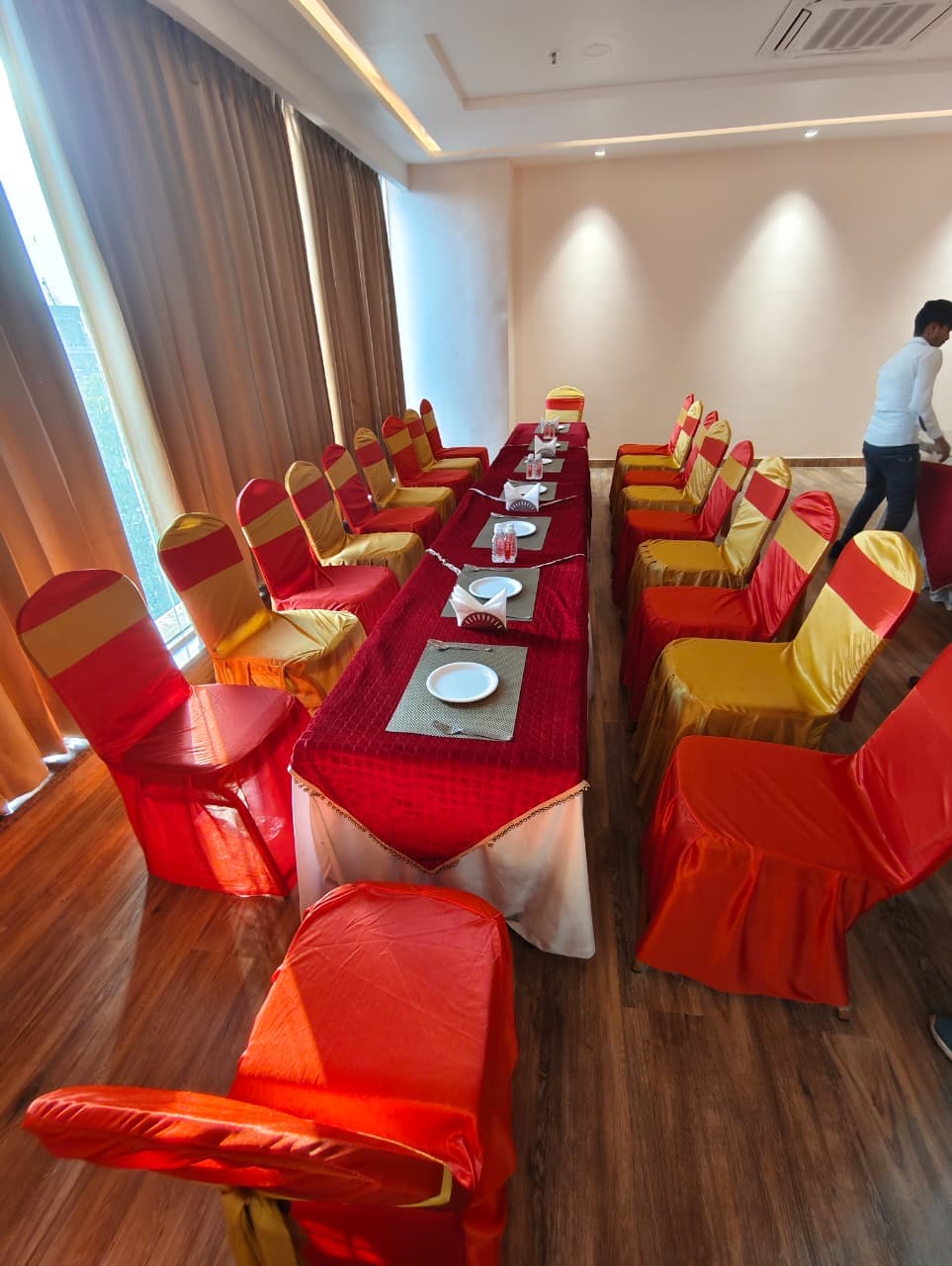 Long banquet table with red tablecloth and chairs with red and gold fabric covers.