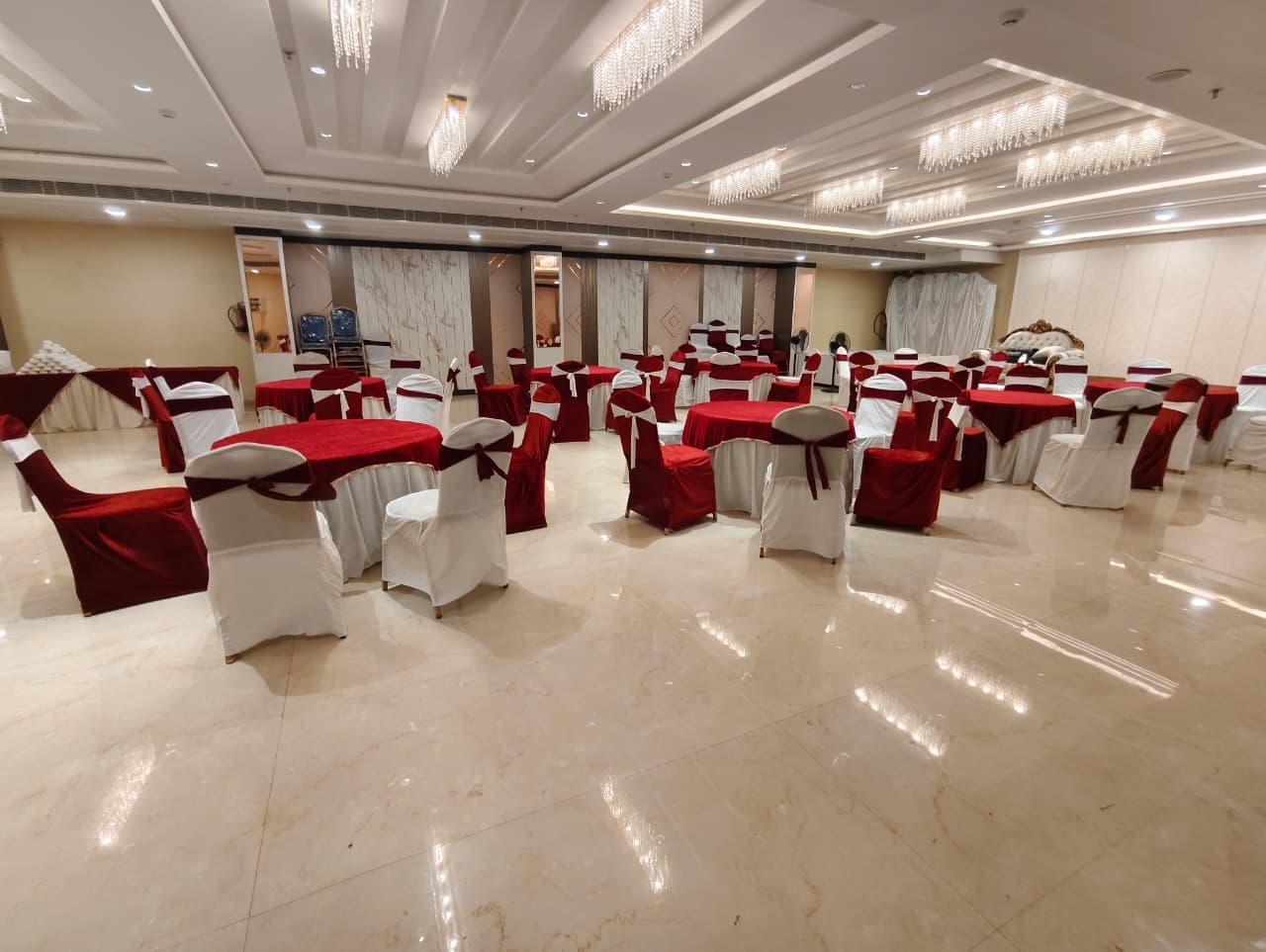 Elegant banquet hall featuring round tables with red linens and white chairs under crystal chandeliers.